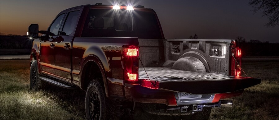 A 2024 Ford Super Duty® truck with available Tremor Package in a dark field with lights on