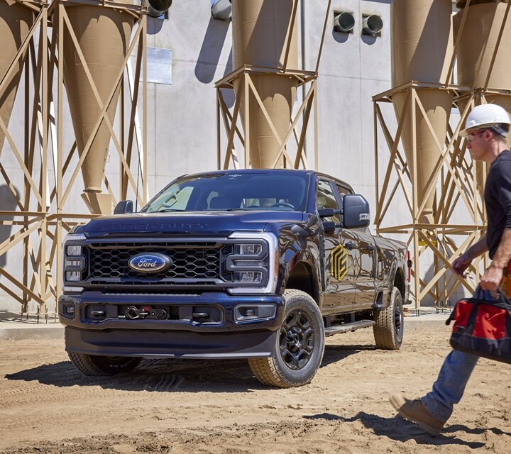A man walking past a 2024 Ford Super Duty® pickup parked near a grain silo