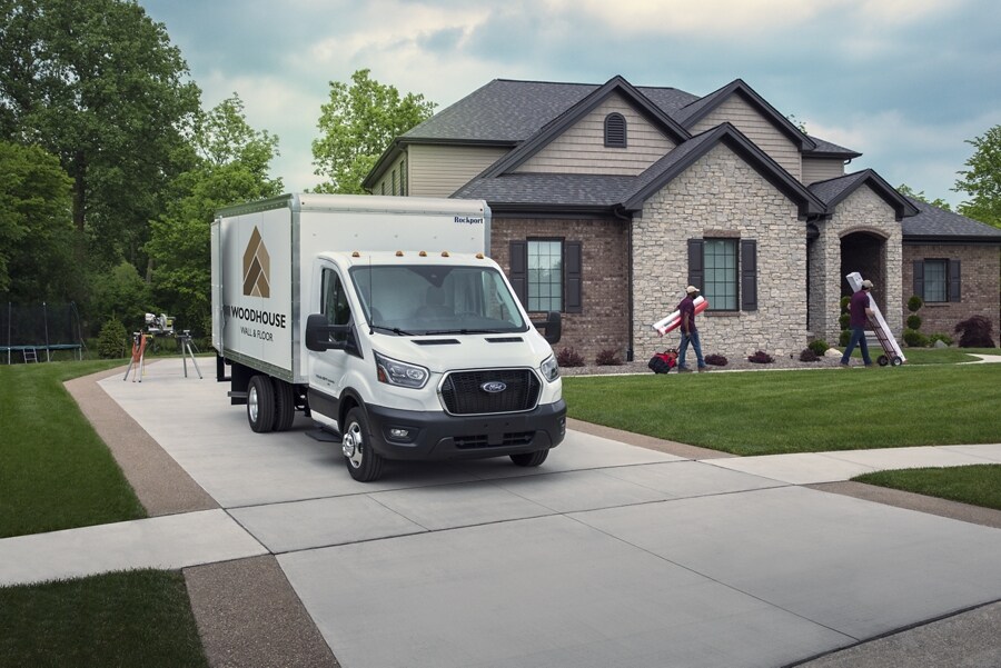 A 2023 Ford Transit® Chassis Cab parked in a driveway of a house with people working