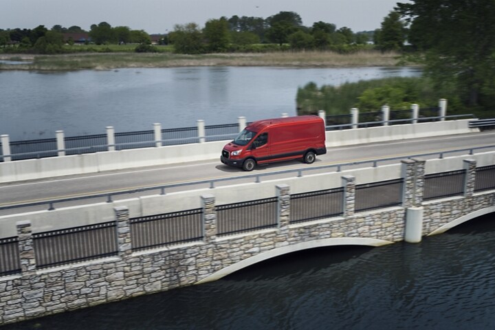 A 2023 Ford Transit® van in Race Red being driven across a bridge