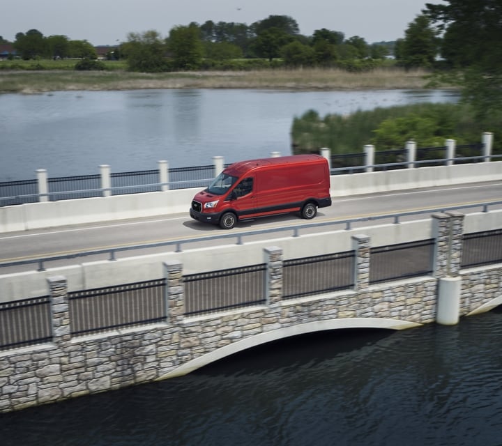 A 2023 Ford Transit® van in Race Red being driven across a bridge