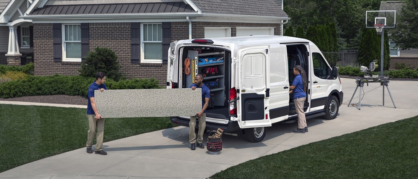 A 2023 Ford Transit® van parked at a home with two men taking a piece of drywall out of the back