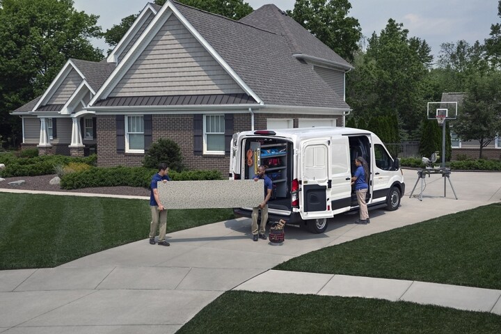 Rear view of a 2023 Transit® Cargo van parked in a driveway with the side and rear cargo doors open