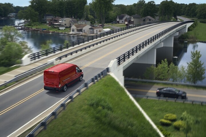 A 2023 Ford Transit® van in Race Red being driven across a bridge