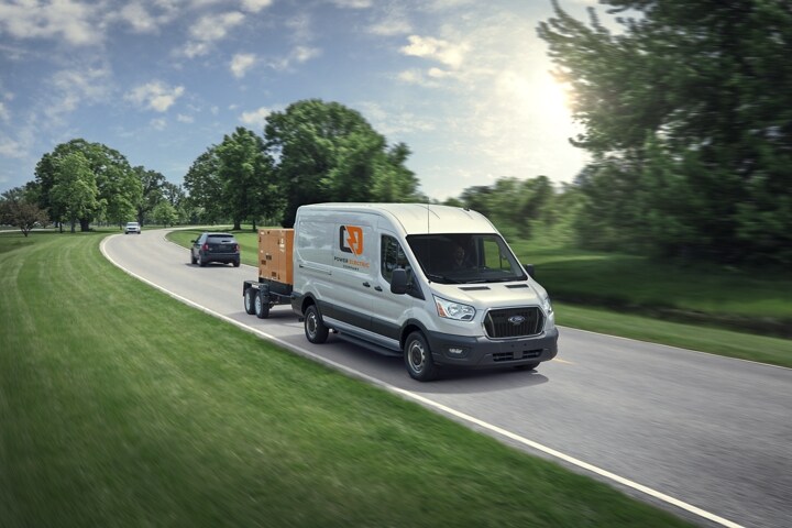 A 2023 Ford Transit® van towing a portable industrial generator on a suburban street