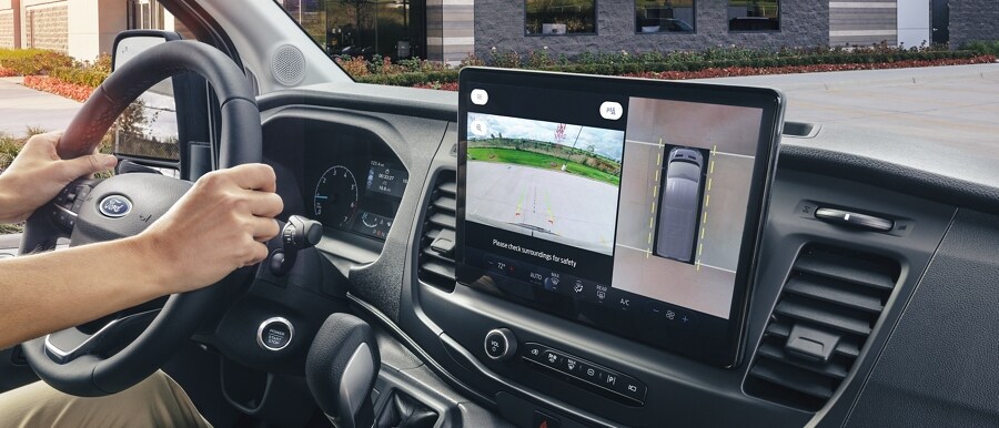 Interior of a 2023 Ford Transit® Cargo Van with driver's hands on wheel and screen showing parked position of vehicle