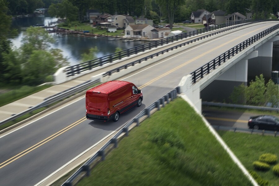 A 2024 Ford Transit® van in Race Red being driven across a bridge