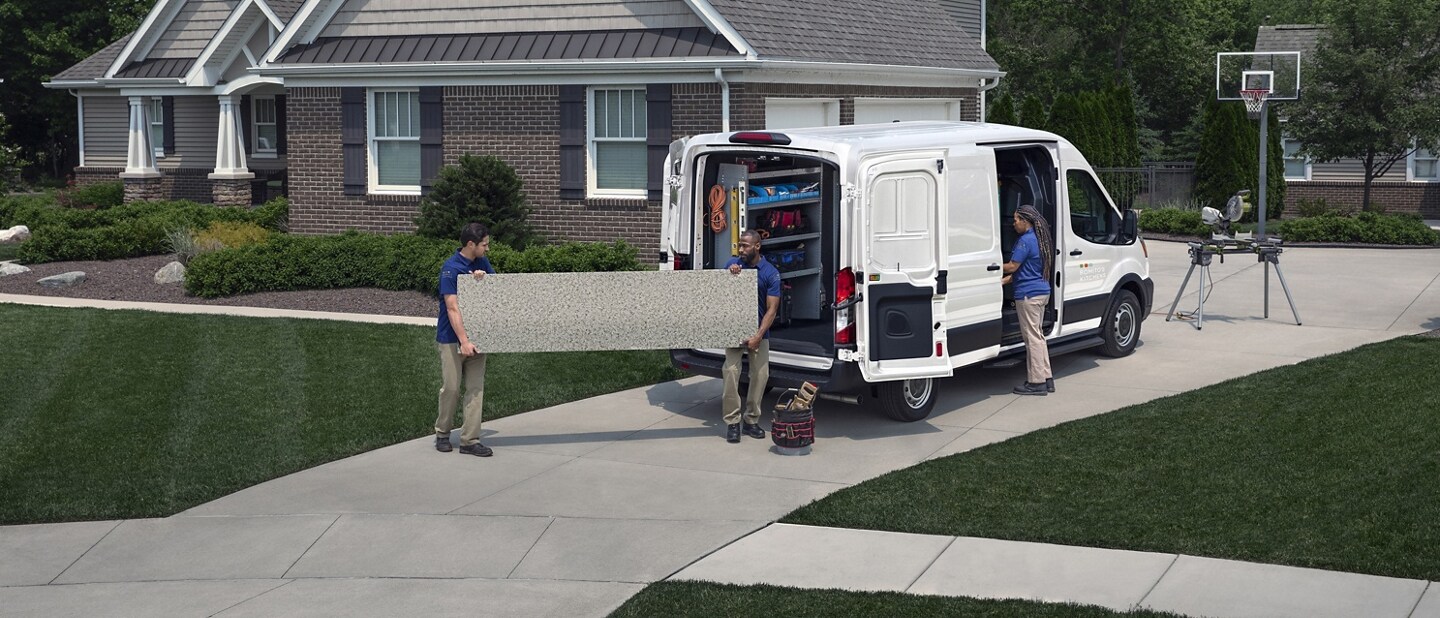 Rear view of a 2024 Ford Transit® Cargo van parked in a driveway with the side and rear cargo doors open