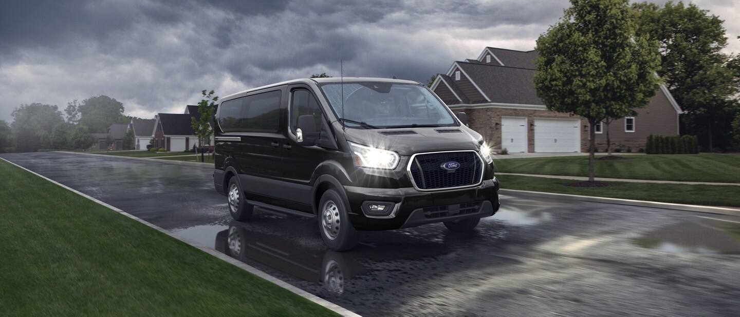 A 2024 Ford Transit® van driving down a wet neighborhood road