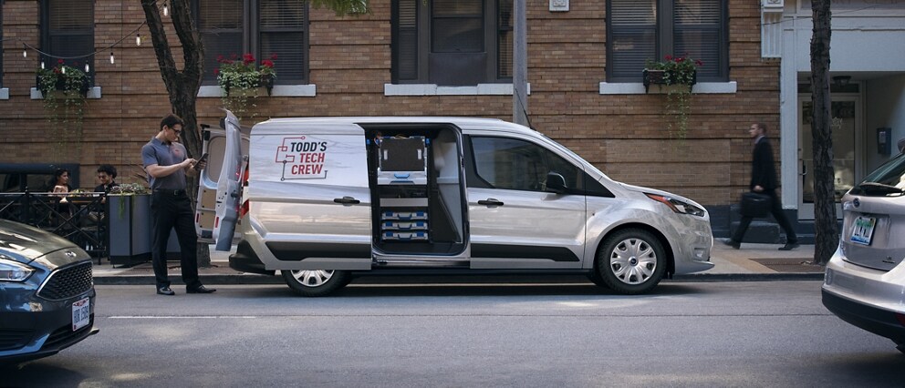 2023 Ford Transit Connect Cargo Van parked in the city shown with available rear swing-out doors and sliding side door open