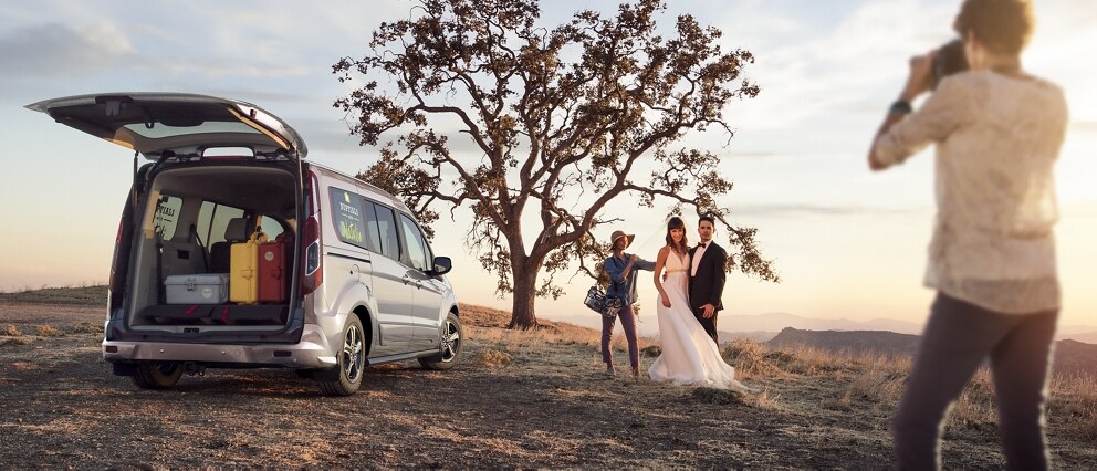 A bride and groom being photographed next to a 2023 Ford Transit Connect Cargo Van in the desert