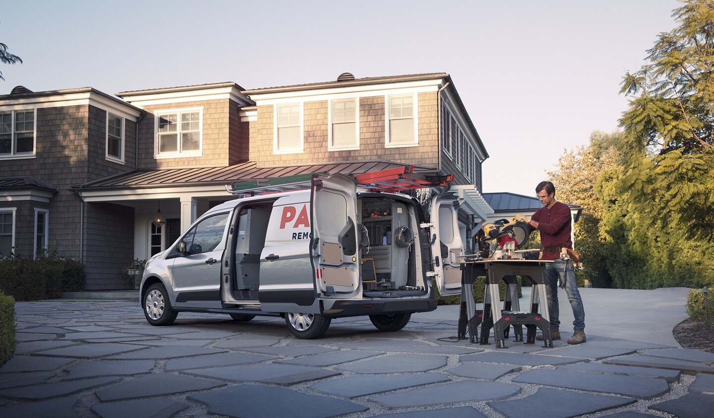 Se muestra una Ford Transit Connect Cargo Van 2023 en Silver con una persona que trabaja en frente de una casa