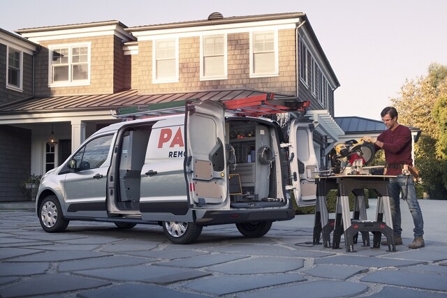 Se muestra una Ford Transit Connect Cargo Van 2023 en Silver con una persona que trabaja en frente de una casa