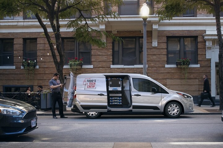 Una Ford Transit Connect Cargo Van 2023 con las puertas dobles laterales deslizables estándar abiertas estacionada en un calle de ciudad