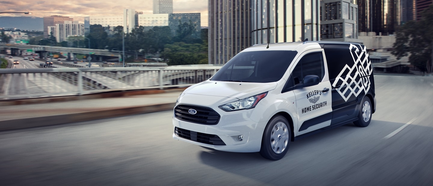 2023 Ford Transit Connect Cargo Van in Frozen White with aftermarket business graphics being driven on a city road