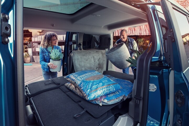 Personas cargando suministros en la zona de carga de una Wagon para Pasajeros Ford Transit Connect 2023 con los asientos plegados de la segunda fila