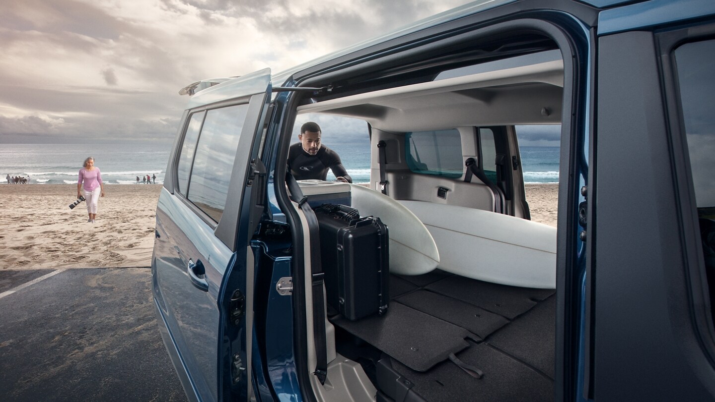 Ample cargo space of 2023 Ford Transit Connect Passenger Wagon shown with a man loading surfboards at the beach