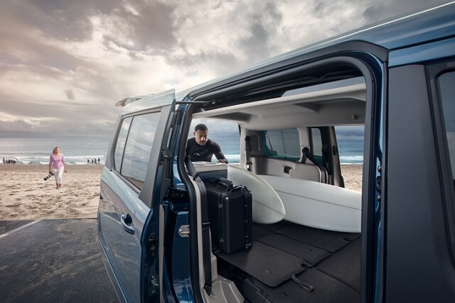 Se muestra el amplio espacio de carga de un Wagon para Pasajeros Ford Transit Connect 2023 con un hombre cargando tablas de surf en la playa