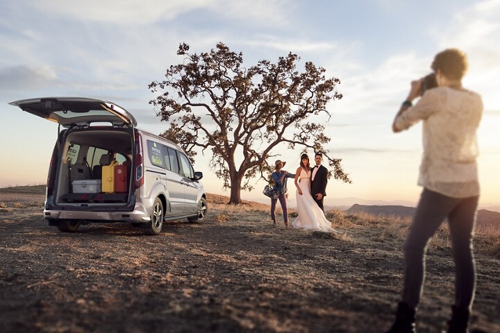 Matrimonio tomando fotos al lado de un Wagon para Pasajeros Ford Transit Connect Titanium 2023 con puerta trasera levadiza disponible