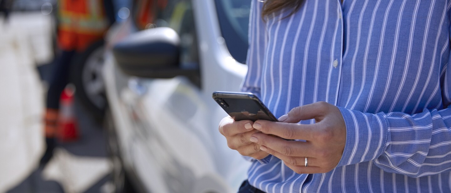 Woman uses smartphone while a technician repairs a tire on her vehicle