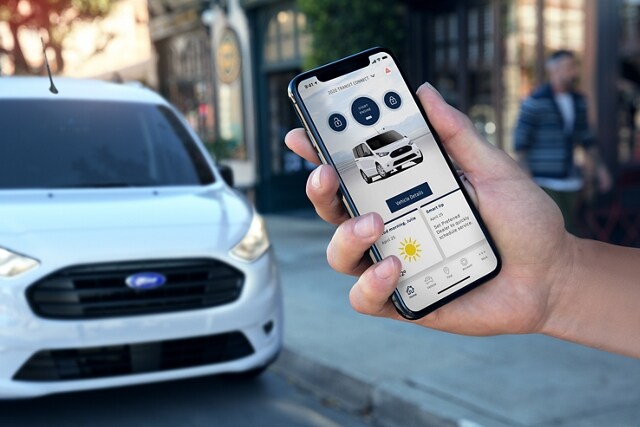 A hand holds a smartphone displaying a 2023 Ford Transit Connect Van within the FordPass™ App
