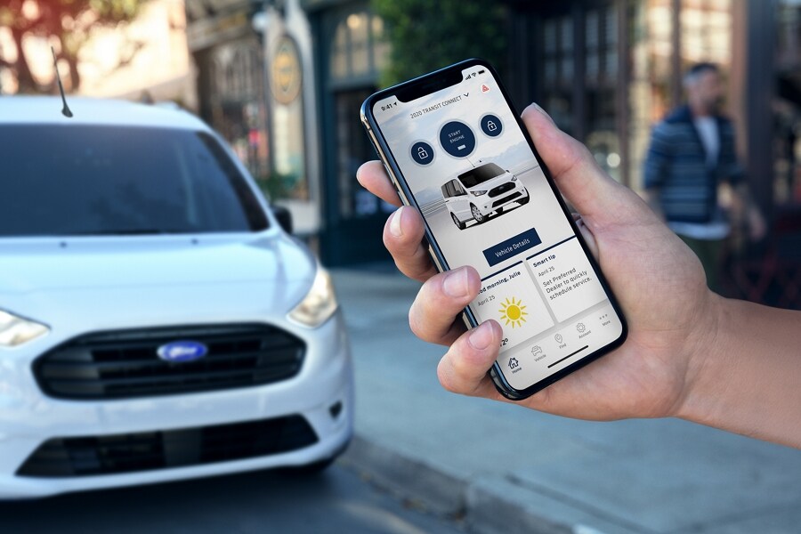 A hand holds a smartphone displaying a 2023 Ford Transit Connect Van within the FordPass™ App