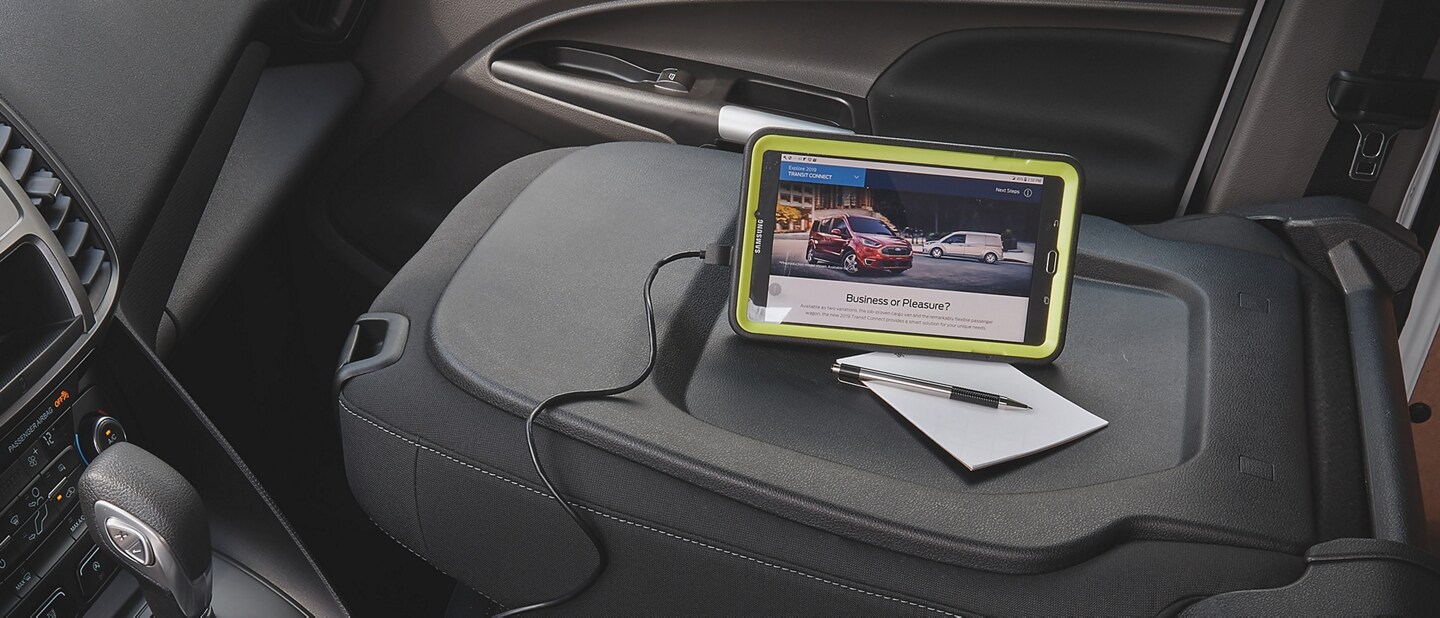 A WiFi tablet rest on the back of a Transit Connects folded passenger seat as it charges using a twelve volt dash socket