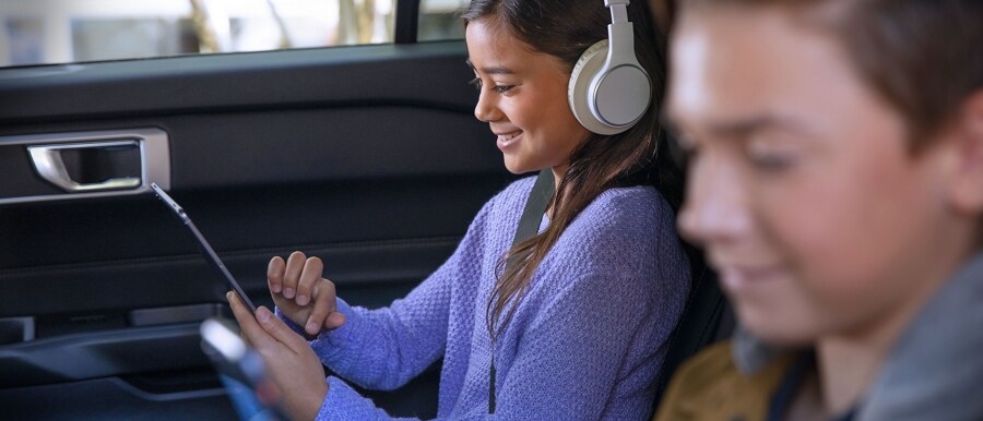 Una niña y un niño usando dispositivos con Wi-Fi en el asiento trasero de un vehículo Ford