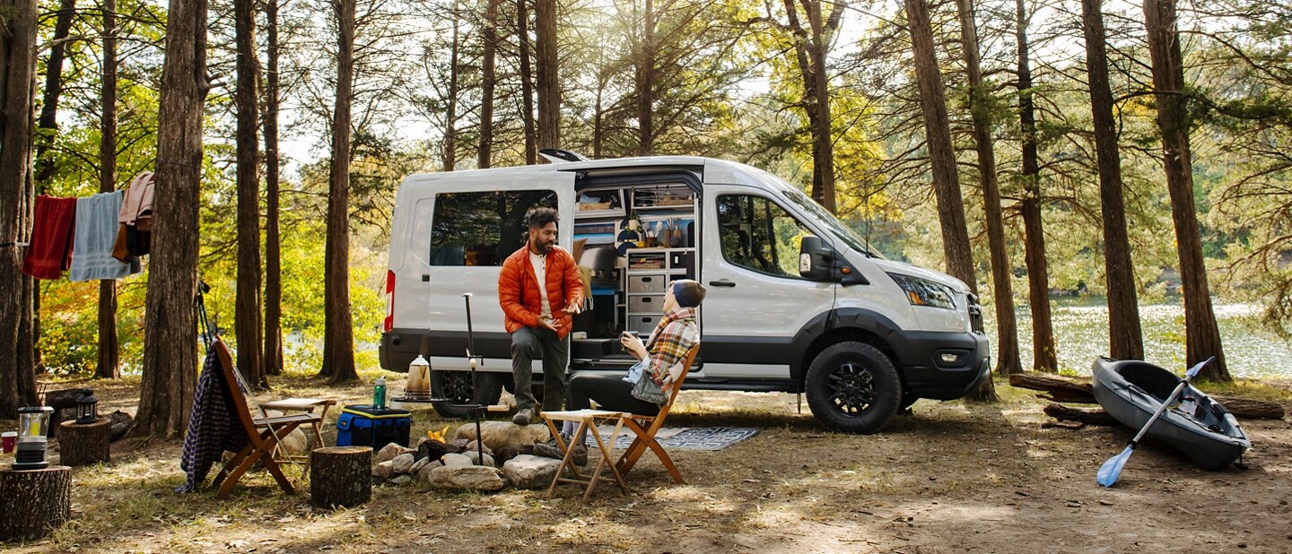 A 2024 Ford Transit® Trail™ Van parked in the woods with a couple camping